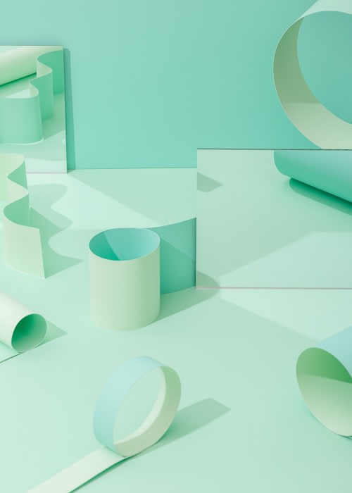 Abstract still life with pastel green geometric paper shapes casting shadows on a light green surface, creating a minimalist composition.