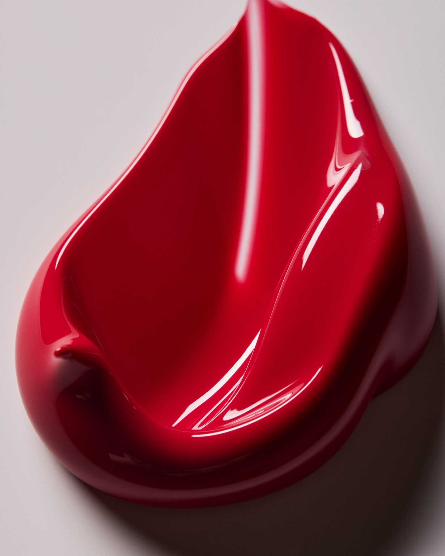 Macro photograph of a vibrant red, glossy cosmetic product smear against a white background, showcasing texture and color details.