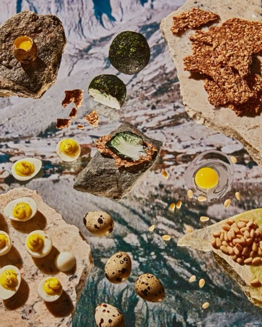 Overhead shot of quail eggs, open egg yolks, and crispy crackers artfully arranged on rocks with a snowy mountain backdrop.