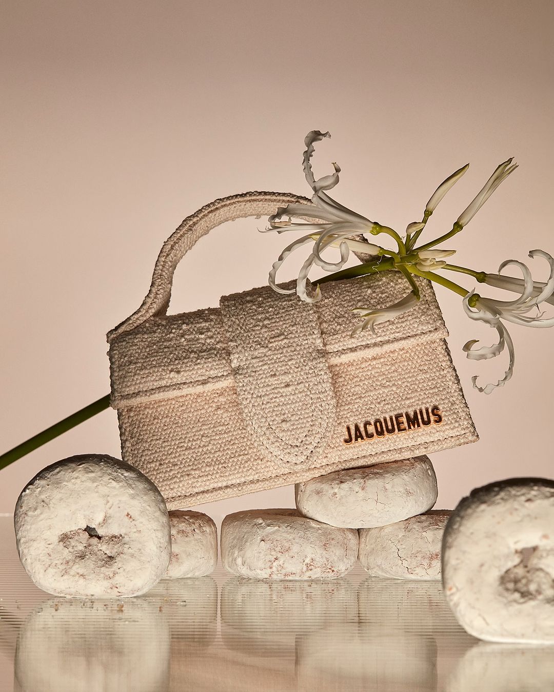 Jacquemus handbag on stack of powdered donuts with white amaryllis flowers in a studio setting with warm lighting. Fashion product shot.
