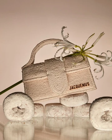 Jacquemus handbag on stack of powdered donuts with white amaryllis flowers in a studio setting with warm lighting. Fashion product shot.