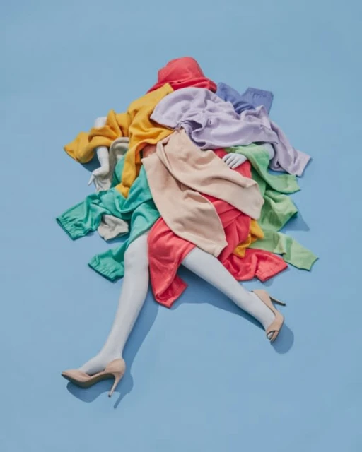 Fashion still life on a blue background featuring a mannequin torso and legs draped in colorful sweaters and skirts with beige heels.