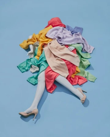 Fashion still life on a blue background featuring a mannequin torso and legs draped in colorful sweaters and skirts with beige heels.