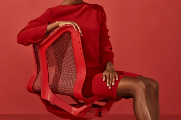 A person in a red dress sits in a red office chair against a matching red background, creating a monochromatic and visually striking image.