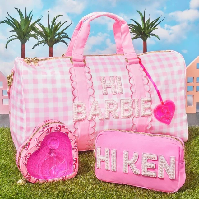 Pink and white gingham duffel bag with matching cosmetic bags on green grass with palm trees and houses in the background.