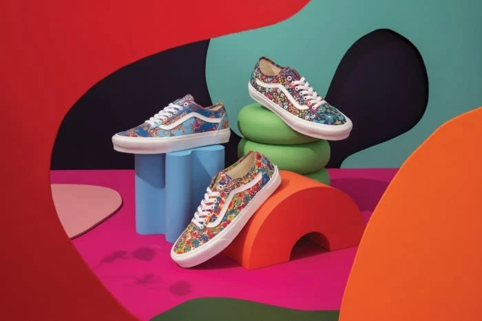 Three floral-patterned Vans sneakers are showcased on colorful geometric platforms against a dark backdrop, creating a vibrant product display.