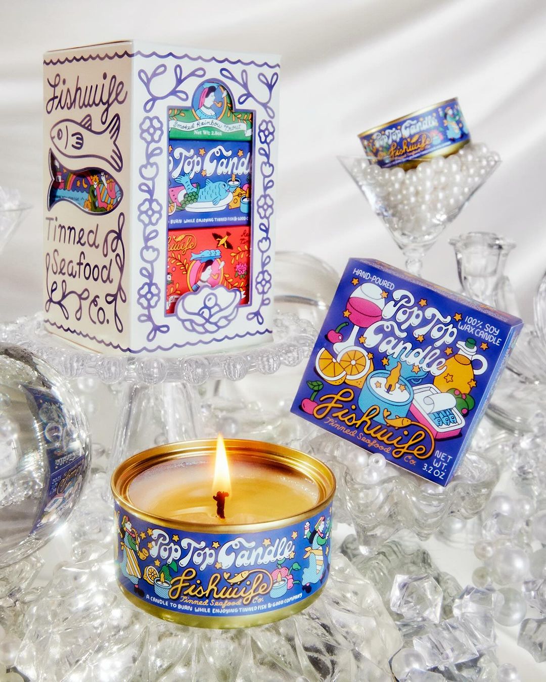 Collection of Pop Top Candle tins and packaging by Fishwife Tinned Seafood Co, featuring vibrant designs, stacked on reflective surface.
