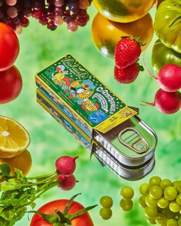 Artistic food still life featuring an open tin of anchovies, tomatoes, lemons, grapes, and radishes on a glossy green surface.