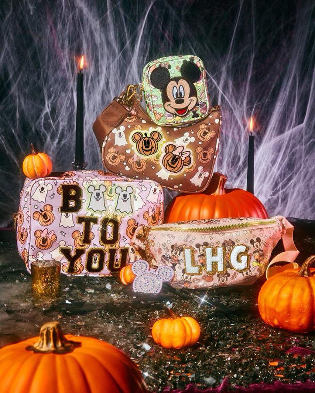 Arrangement of Disney Halloween-themed purses, decorative pumpkins, and candles against a spider web background for a festive display.