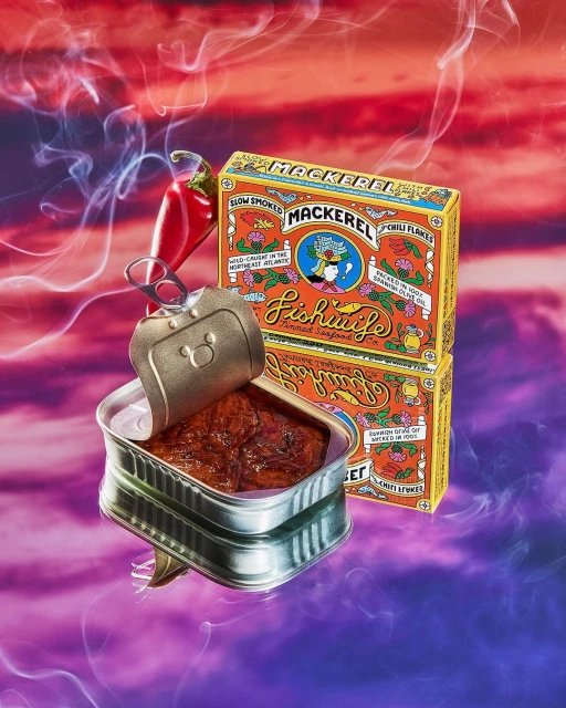 Canned mackerel fillets in a tin, next to stacked product boxes and a fresh red chili, against a vibrant abstract background.