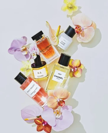 Flat lay of multiple designer perfume bottles arranged among fresh orchids and flowers on a white background by Stephanie Gonot.
