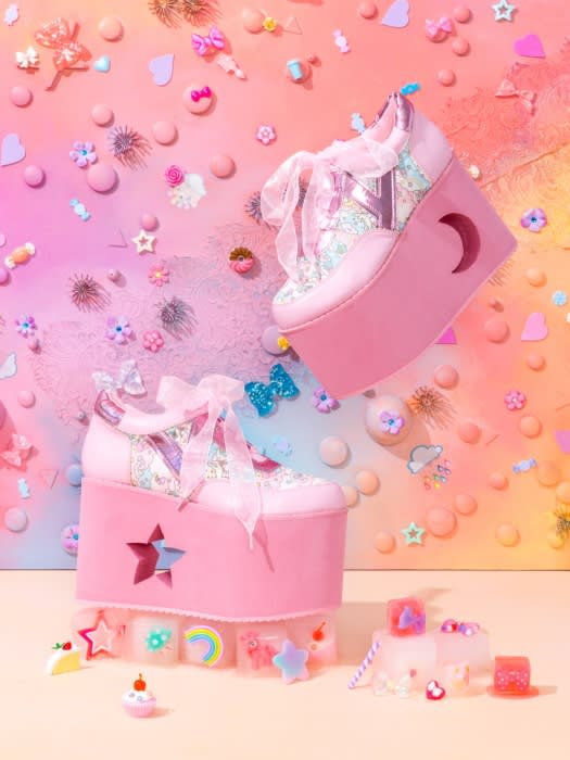 Pastel pink platform shoes with star and moon cutouts, ribbons, and whimsical decorations against a multicolored background.
