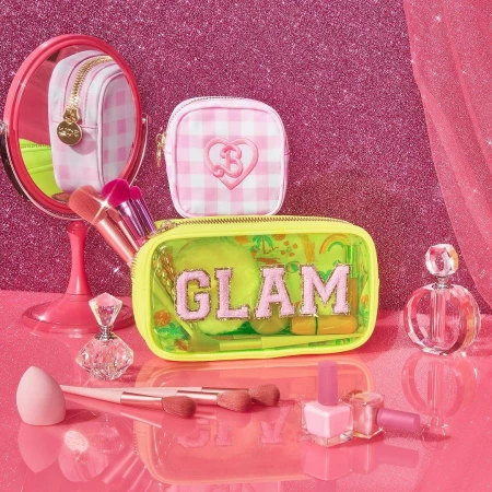 Glamorous beauty product presentation featuring makeup bags, brushes, nail polish, and perfume in a pink setting with glitter backdrop.