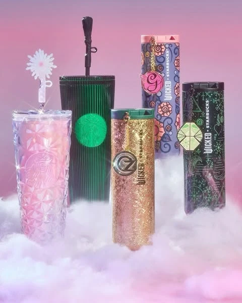 Collection of Wicked-themed Starbucks tumblers in green, gold, pink, and purple colors arranged in a studio setting with dreamy lighting.