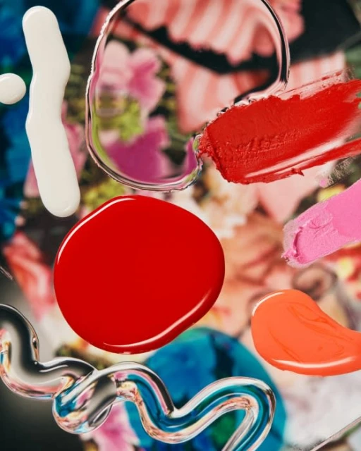 Abstract close-up of red, orange, pink, and white paint swatches and clear gel over a blurred multicolored floral background.
