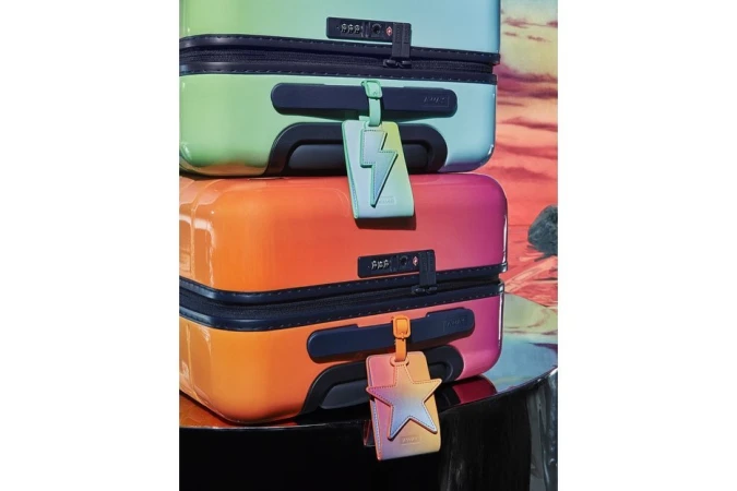 Stack of colorful hard shell suitcases with a lightning bolt and star luggage tag in a studio setting against a desert background.