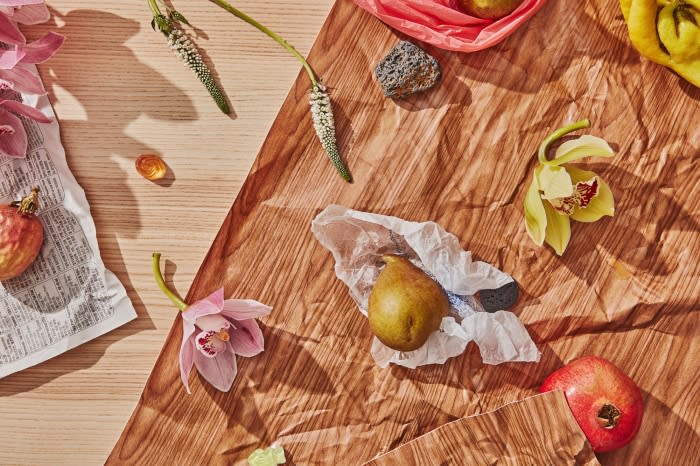 Still life composition featuring pears, pomegranates, and orchid flowers on a textured brown paper background, shot with natural lighting.