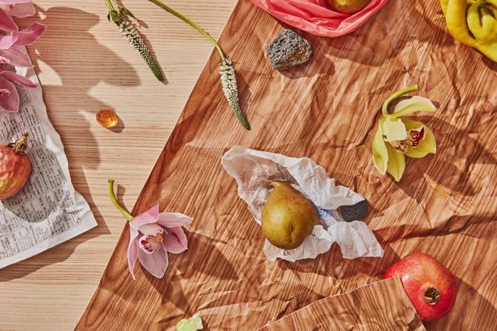 Still life composition featuring pears, pomegranates, and orchid flowers on a textured brown paper background, shot with natural lighting.