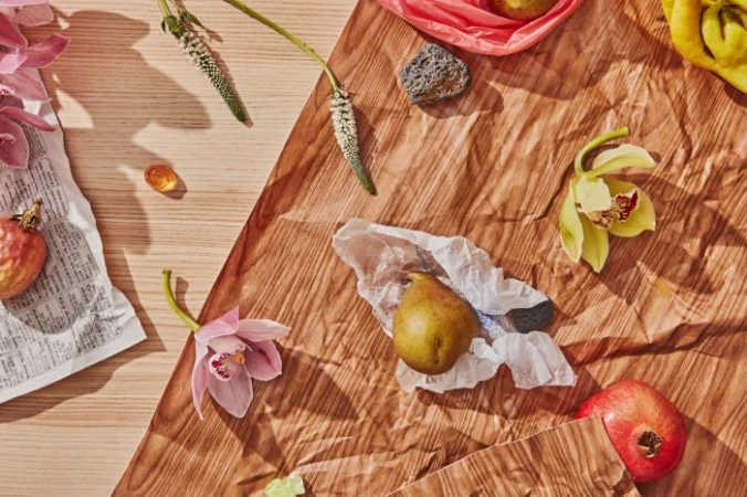 Still life composition featuring pears, pomegranates, and orchid flowers on a textured brown paper background, shot with natural lighting.