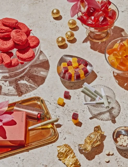 Overhead still life featuring edible cannabis products, including gummies, cookies, and pre-rolls arranged on a light-colored surface.