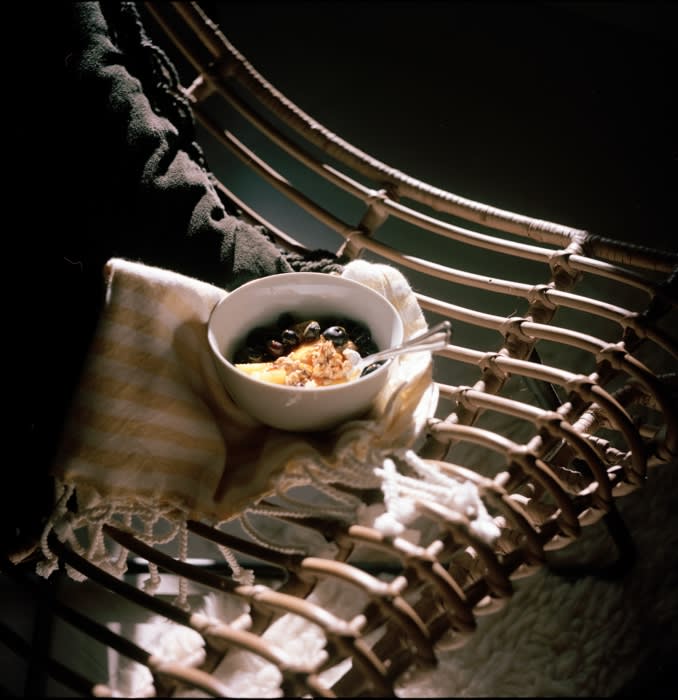 A bowl of fruit and granola on a striped towel draped over a wicker chair, creating a cozy and inviting food still life.