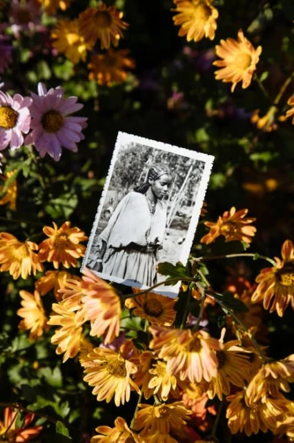 Monochrome portrait photo of a woman surrounded by vibrant orange and pink flowers, adding a layer of nostalgia and natural beauty.