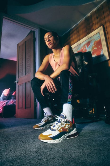 A young adult sits on a chair with neutral carpet and wooden walls in an indoor setting, showcasing off-white and brown sneakers.