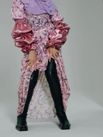 Model wearing a pink patterned dress with satin balloon sleeves and black leather boots against a white background