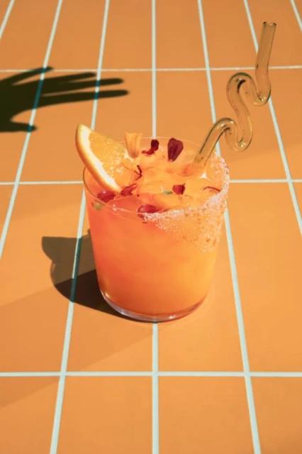 Close-up of a refreshing orange cocktail with a whimsical straw, garnished with an orange slice, set against a vibrant orange tile backdrop.