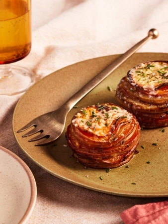 Close-up of two potato stacks with melted cheese and herbs on a green plate with a golden fork next to a glass of beer.