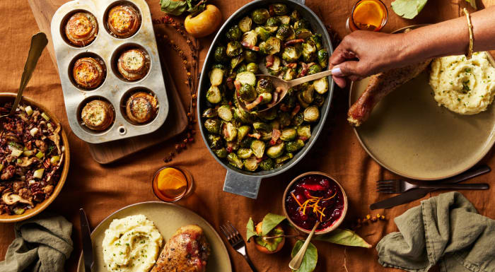 Overhead shot of a Thanksgiving table with stuffed mushrooms, Brussels sprouts, cranberry sauce, turkey, and mashed potatoes.