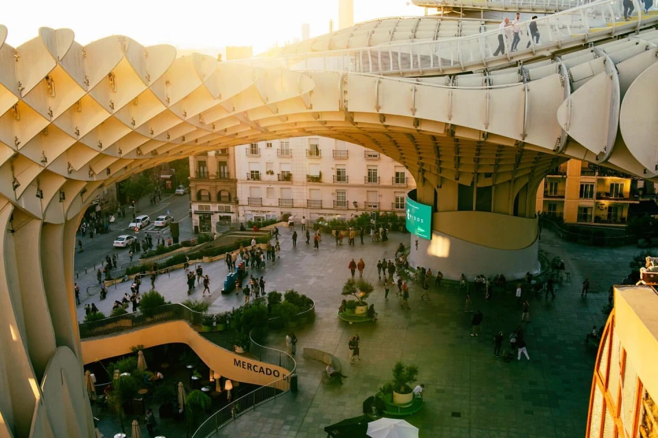 Metropol Parasol in Seville, Spain, a wooden waffle-like structure, with people walking below and on its elevated walkway at sunset.