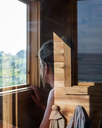 Woman looking out a wooden cabin window, captured by photographer Gabriela Herman.