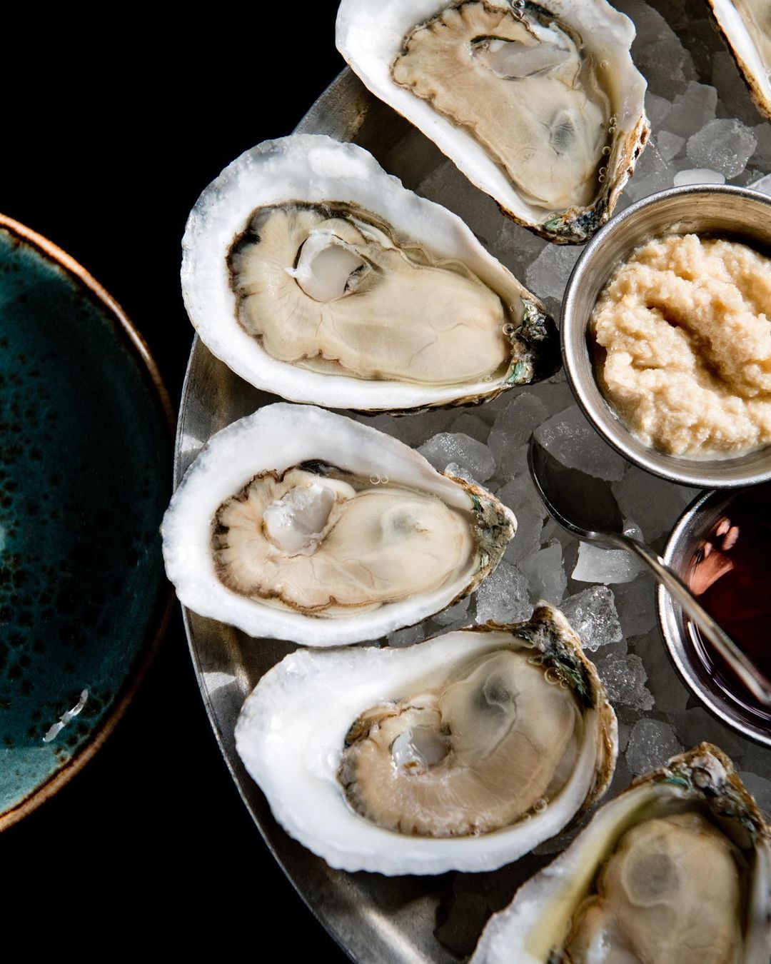 Overhead shot of fresh oysters on ice with small bowls of mignonette sauce and horseradish on a silver platter, elegant seafood dining.