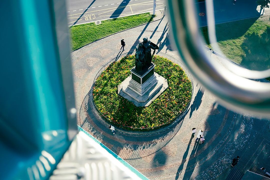 High-angle view of a public park with a statue, walking paths, and greenery, captured from an elevated position, showcasing urban park design.