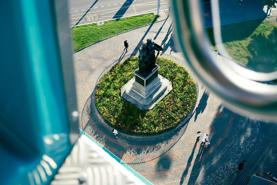 High-angle view of a public park with a statue, walking paths, and greenery, captured from an elevated position, showcasing urban park design.
