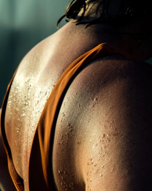 Close-up shot of the back of a sweaty adult woman with short hair wearing an orange bathing suit strap. Studio lighting is used.