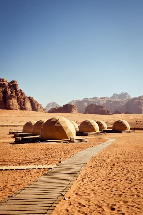Desert glamping resort with domed tents, wooden walkway, and mountains in the background on a clear day in Wadi Rum, Jordan.