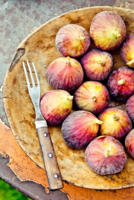 Close-up of fresh figs arranged on a wooden plate with a fork, showcasing the fruit's vibrant colors and rustic presentation.