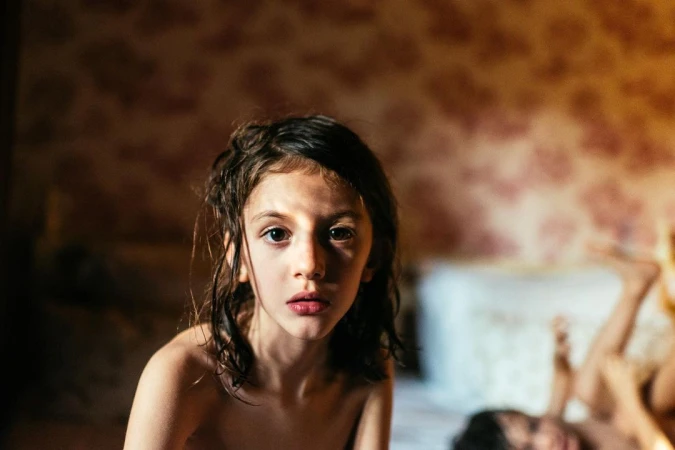 Close-up portrait of a child with dark hair looking at the camera against a patterned wall, photographed by Gabriela Herman