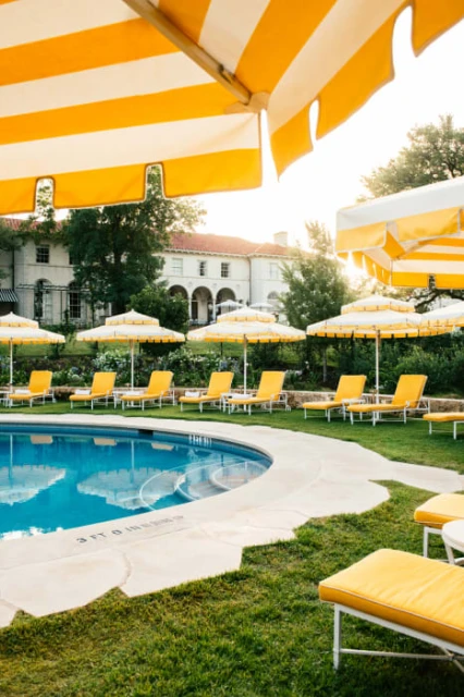 Swimming pool lined with yellow lounge chairs and parasols with a white building in the background during the daytime.
