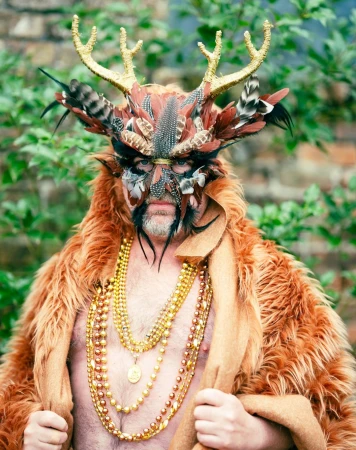 Portrait of a man wearing an elaborate feathered headdress with gold antlers and layered gold bead necklaces by Gabriela Herman