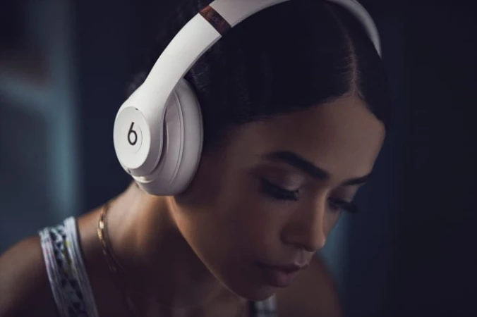 Young woman wearing white Beats headphones with her head down, set against a softly blurred background. Close-up shot, indoor setting.