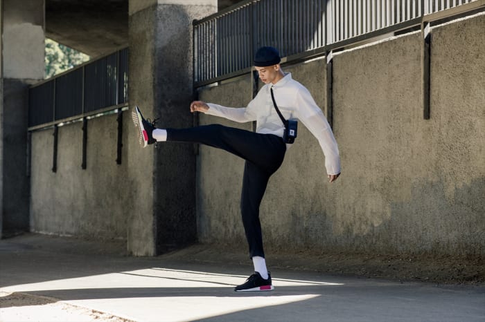 A young adult in athletic attire practices a dynamic kicking pose in an urban environment, highlighting movement and contemporary fashion.