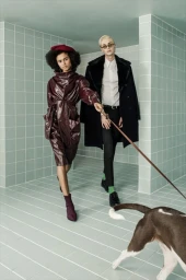 Two models posing in a tiled green room with a dog on a leash, styled by wardrobe stylist Jessie Jamz.