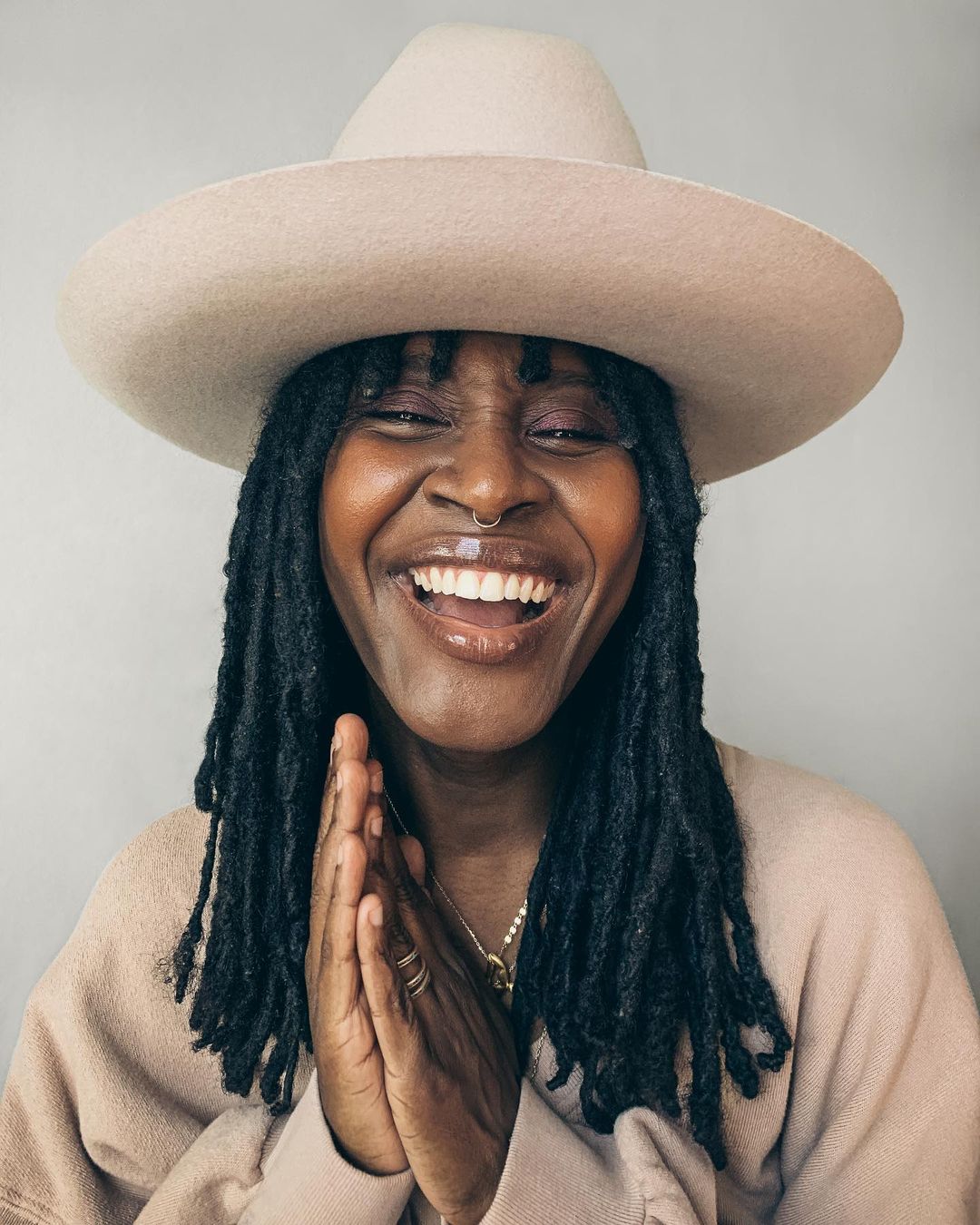 Smiling woman with dreadlocks and a hat with hands together. Close-up studio portrait of a smiling adult woman wearing a wide-brimmed hat.
