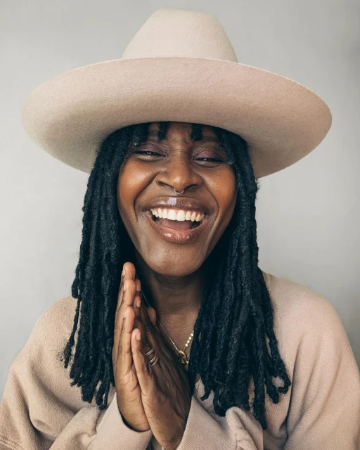 Smiling woman with dreadlocks and a hat with hands together. Close-up studio portrait of a smiling adult woman wearing a wide-brimmed hat.