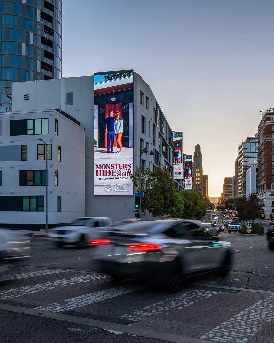 Urban landscape featuring a large billboard on a building with two people, traffic moving on the street, and modern architecture.