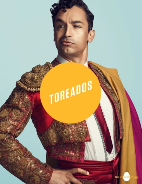 Portrait of a handsome adult male wearing an ornate matador costume in a studio against a pale blue background with a serious expression.