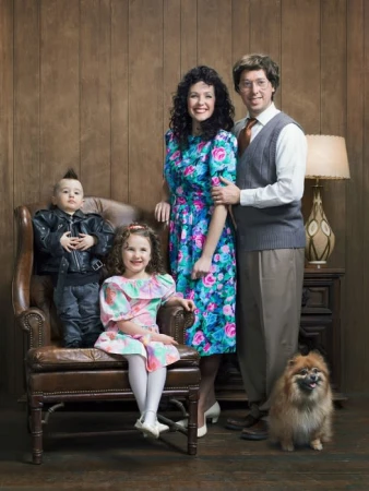 Family portrait in 1980s style features parents, two children, and a dog indoors with wood-paneled walls and vintage furniture and clothing.